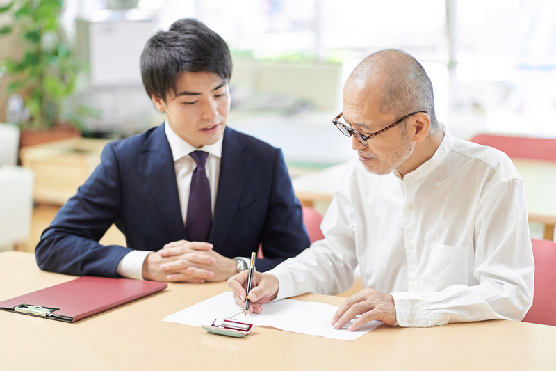 An elderly man signing legal documents with a professional, related to Grant of Probate in Singapore.